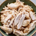 Close-up of boiled chicken strips arranged in a green ceramic bowl.