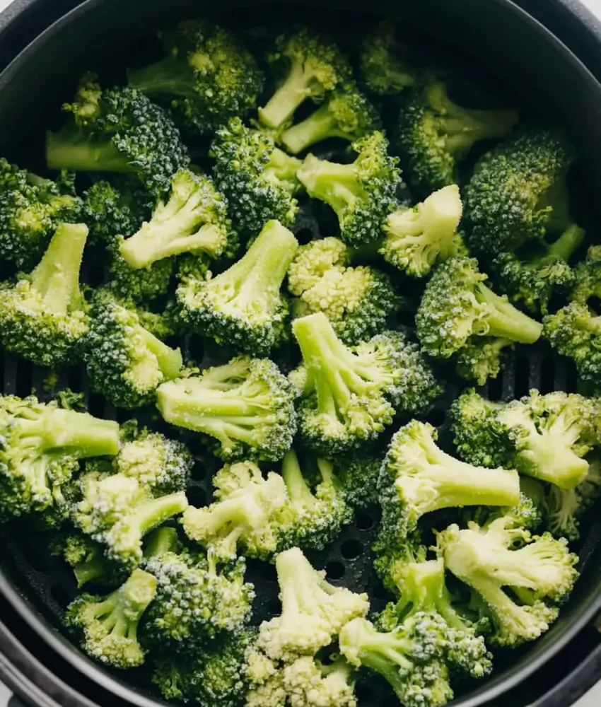 Frozen broccoli florets arranged in an air fryer basket, ready to cook.