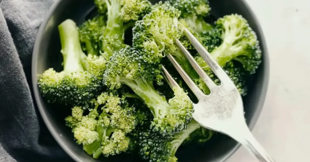 Close-up of air-fried frozen broccoli in a dark bowl with a silver fork.