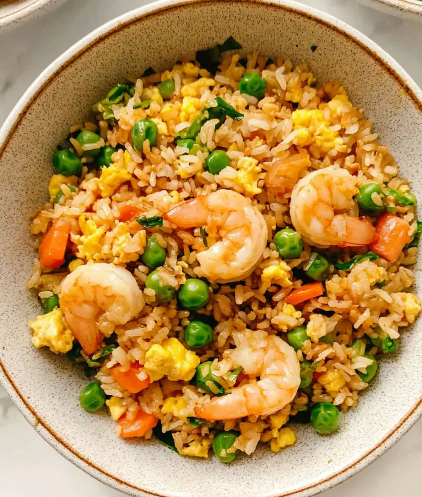 A skillet filled with fried rice, shrimp, spinach, scrambled eggs, and peas.