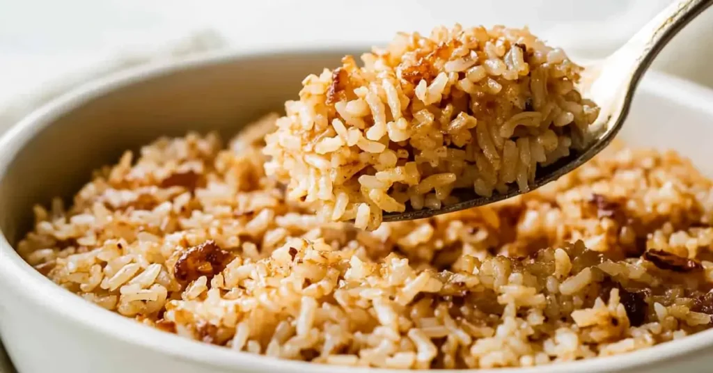 a close-up of "stick of butter rice," featuring fluffy white rice cooked to a golden brown with visible crispy edges. A spoon lifts a generous portion, showcasing the rich, buttery texture and evenly browned bits, likely caramelized for added flavor.