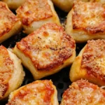 Close-up of golden brown frozen pizza bites cooked in an air fryer, topped with melted cheese and seasonings.