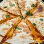 Golden-brown air fryer quesadilla sliced into triangles, filled with melted cheese and garnished with fresh cilantro, served on a black plate.