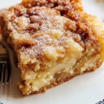 A slice of moist cinnamon sugar apple cake served on a white plate with a decorative black border, dusted with powdered sugar and showing layers of apples and crumb topping.