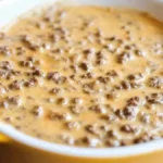 A close-up of creamy hamburger dip in a yellow baking dish, featuring ground beef and melted cheese.