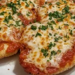 Golden breaded chicken breasts topped with marinara sauce, melted mozzarella cheese, and fresh parsley, served on a white plate.