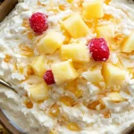 A bowl of creamy pineapple fluff dessert topped with diced pineapple and raspberries.