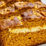 Close-up of a freshly baked pumpkin cream cheese bread with a golden brown crust and a creamy filling in the center.
