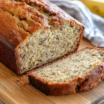 A freshly baked banana bread loaf with a golden crust and soft interior, placed on a wooden cutting board