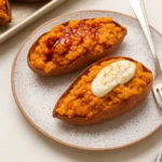 Twice-baked sweet potatoes filled with mashed sweet potato, drizzled with maple syrup and topped with whipped cream, served on a speckled ceramic plate